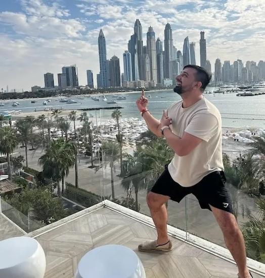 Matt Sheikh standing on a building on the water with the city in the background.