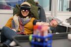 A person reclined and donating blood. They are wearing a VR headset and smiling.