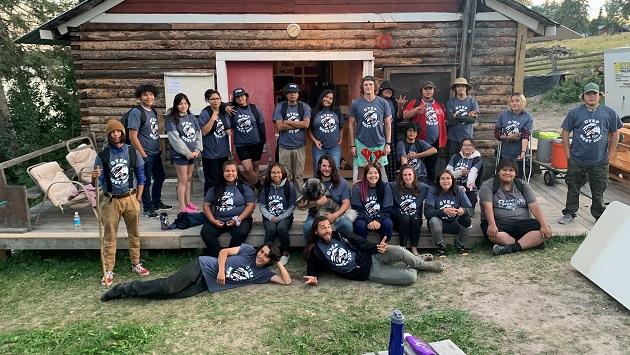 A group of youths in front of a log cabin 