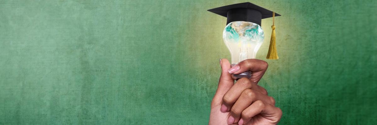 Hand holding a lightbulb with a graduate mitre on top of the bulb.