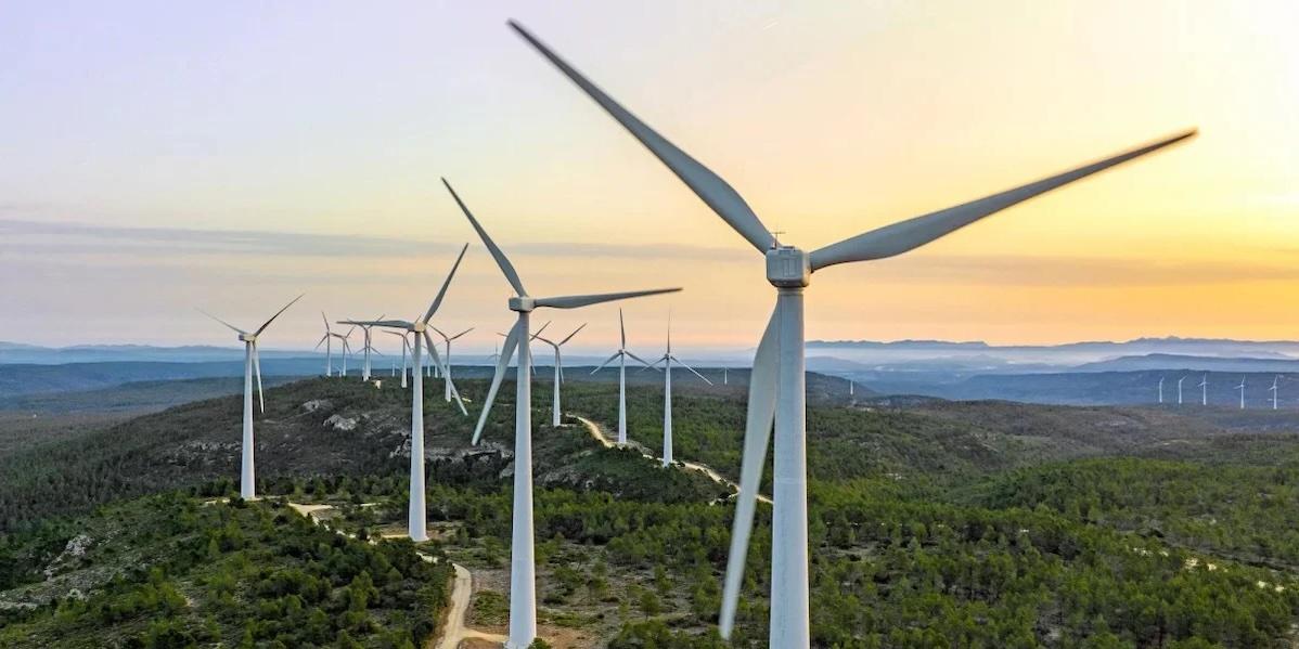 Windmills on top of a hill with the sun setting in the background.