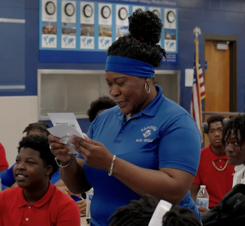 Woman reading a letter to a class of students. 