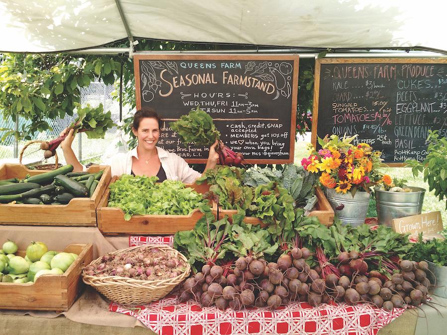 Person sitting at a farm stand covered in vegetables at Queens County Farm Museum