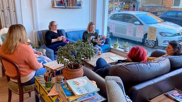 A group of people seated on couches and chairs, some holding mugs or food.