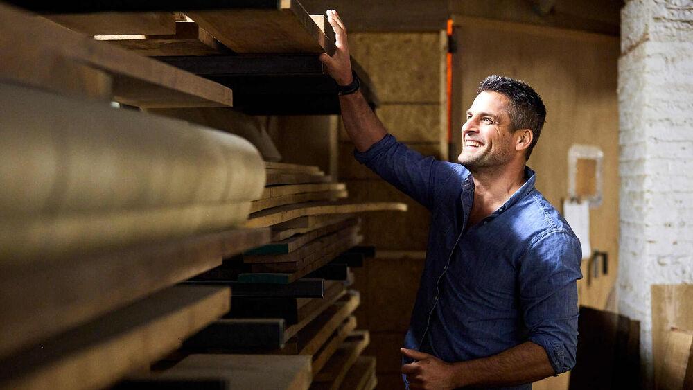 A smiling person selecting a piece of lumber from a rack.