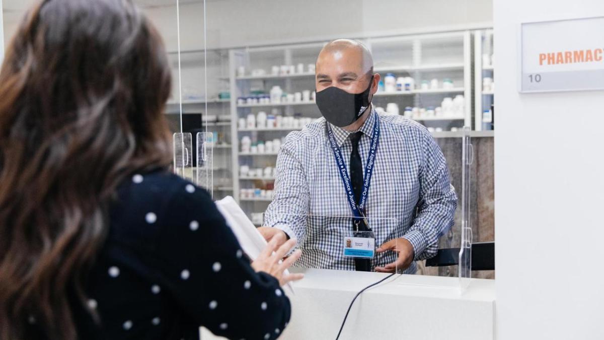 A pharmacy health worker hands a prescription to a patient.