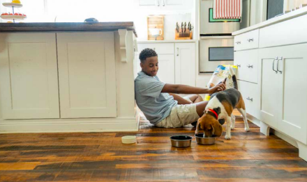 A child sits alongside a dog while the dog is eating 