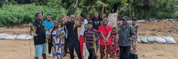 A group of smiling people posed outside, holding plants.