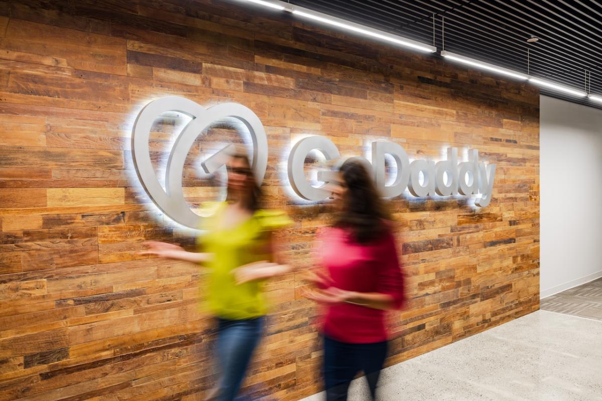 Two GoDaddy teammates in front of a GoDaddy sign.