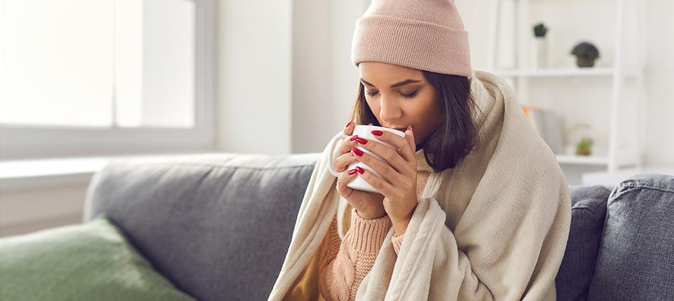 women drinking from a mug wrapped in a hat and blanket