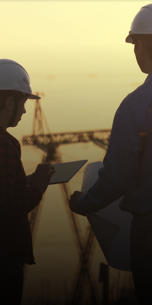 Two professionals wearing safety hats looking at a tablet and piece of paper