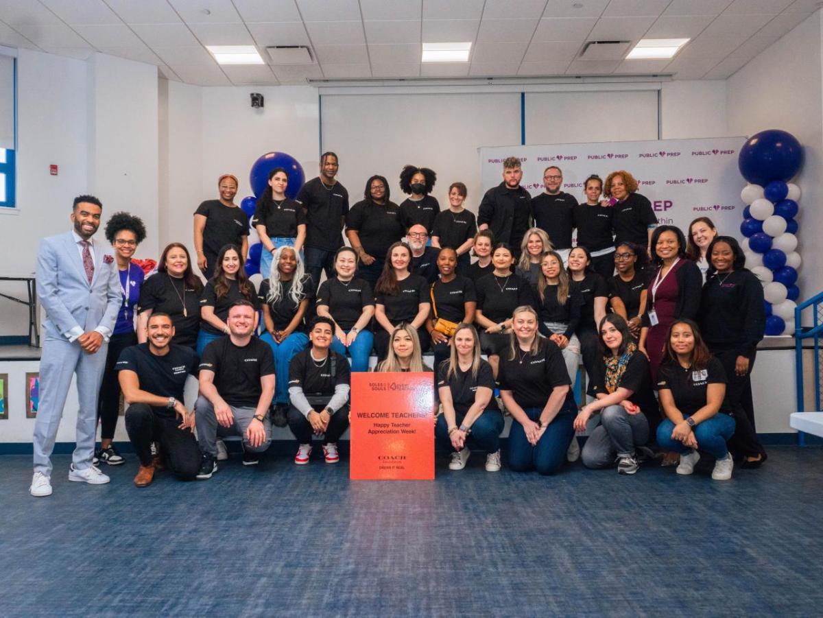 A group of me and woman wearing black shirts stand and kneel looking directly at the camera