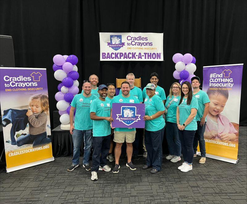 A group of volunteers posed together, some holding a sign "Cradles to Crayons" signs to the sides and behind them for Cradles to Crayons and Backpack-a-thon.