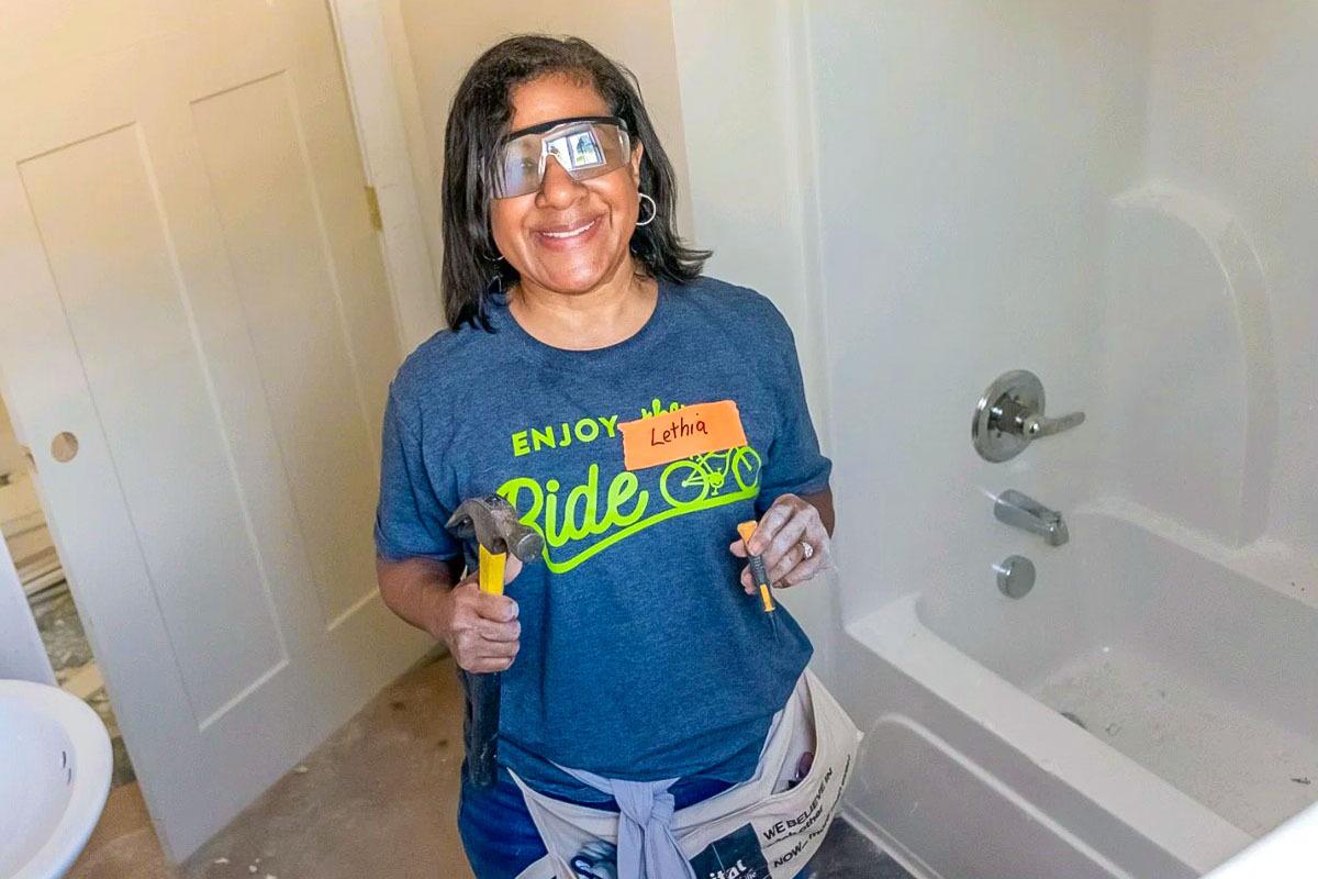 A smiling volunteers holding a hammer.