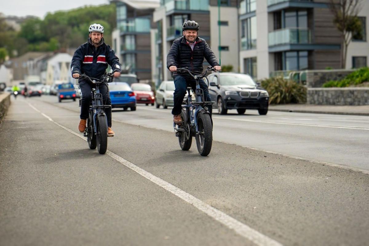 Pete Bowker and Daniel Usher riding e-bikes on a road.