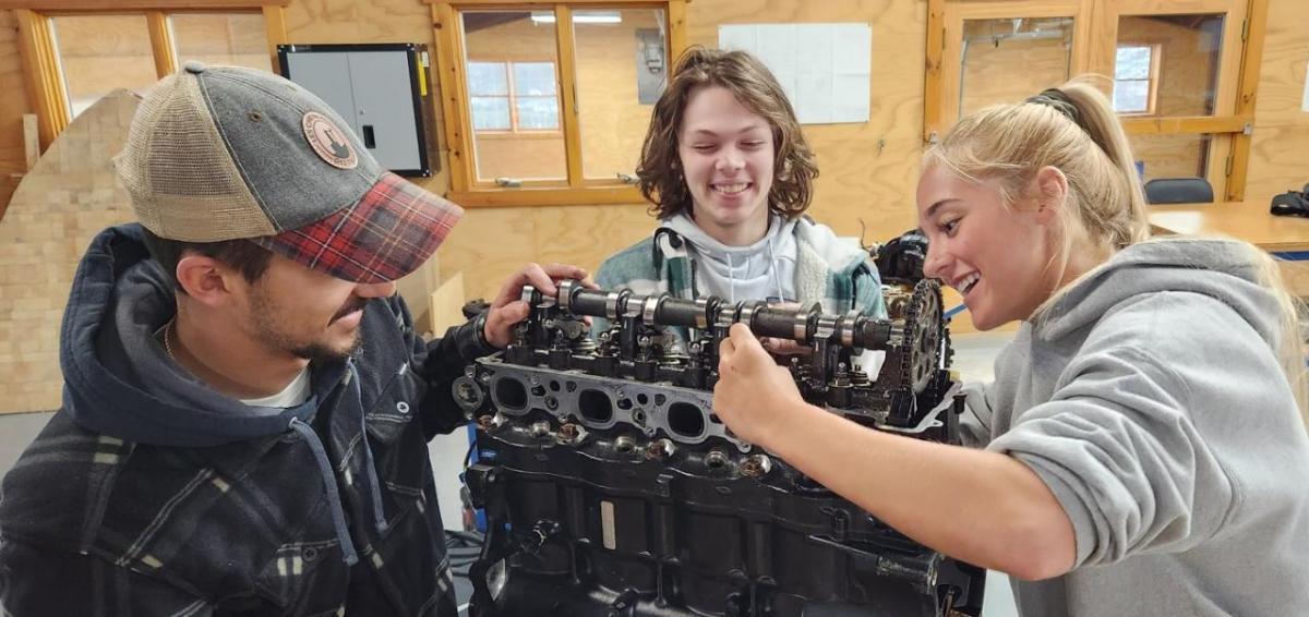 Three smiling people working on a large mechanical piece.