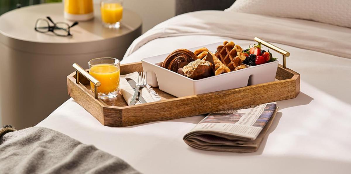 A tray filled with breakfast items, a newspaper tucked underneath, placed on a bed.