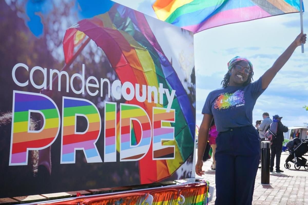 A person waving a pride flag next to a sign that says "Camden County PRIDE"