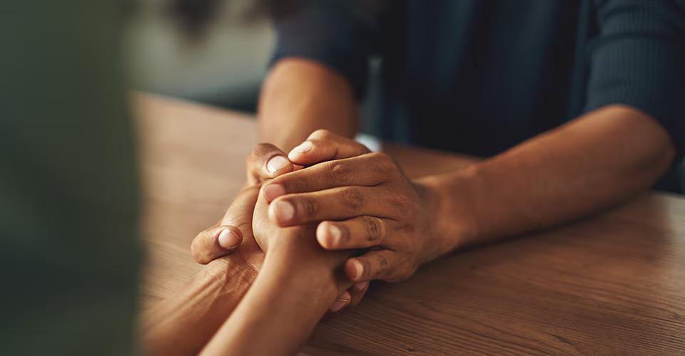 Close up of two people holding hands over a table.