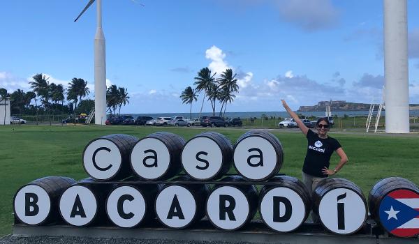 Jessica outside next to barrels spelling out "Casa Bacardi" Wind turbines in a grassy area behind her. Image courtesy of Page