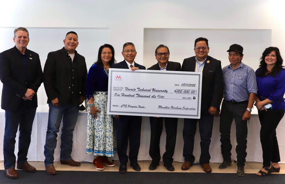 a group of people standing, three holding a large check 