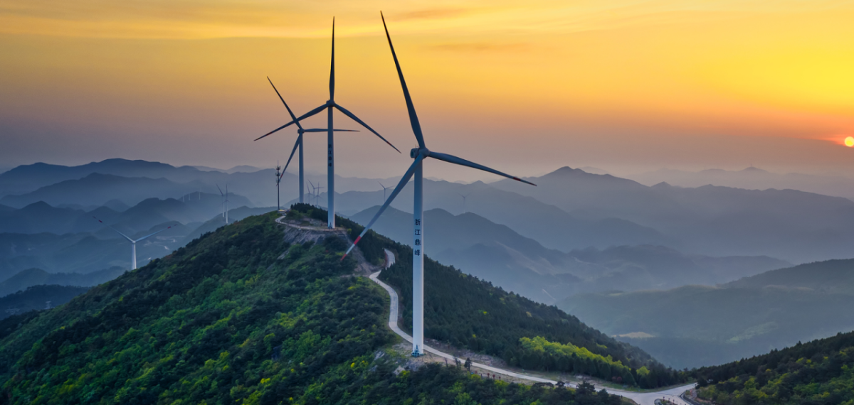 Wind turbines on top of a peak, setting sun in the background