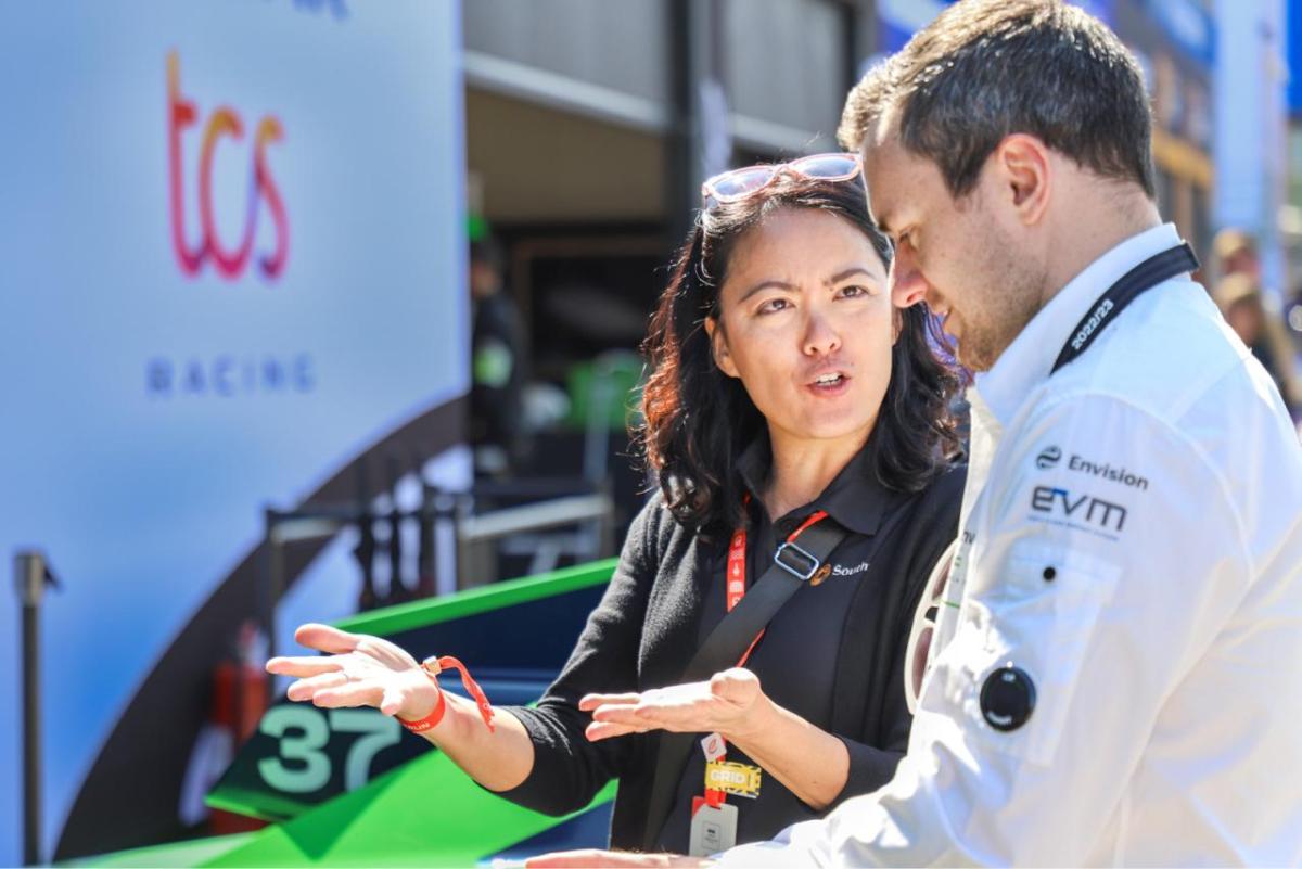 Two people talking, a race car behind them.