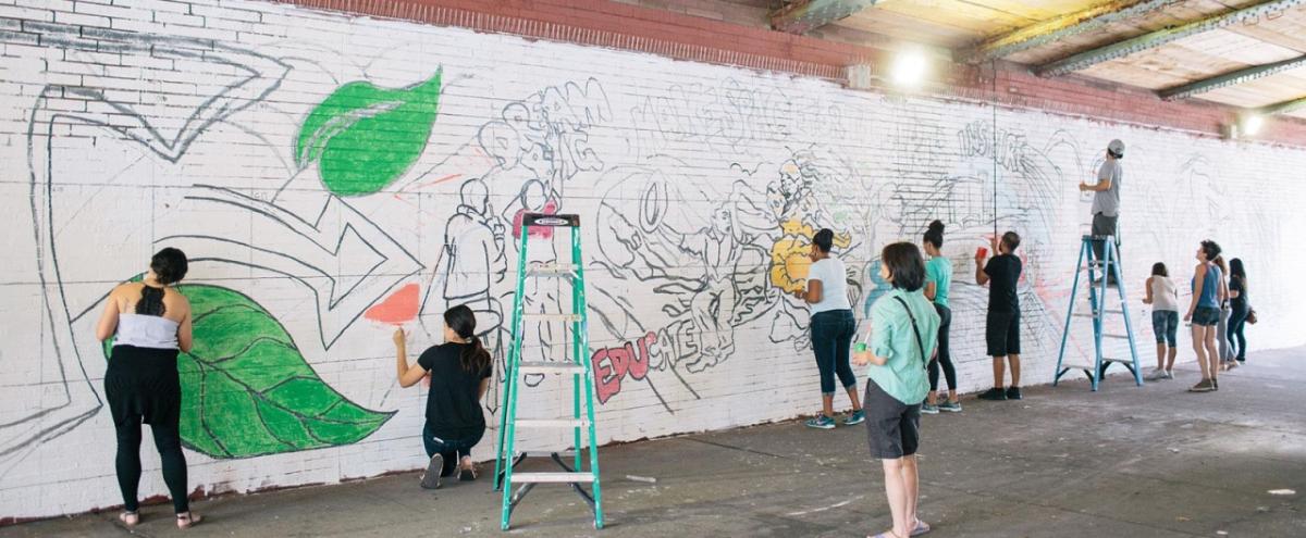 a group of people paint a mural on the wall of an under-pass