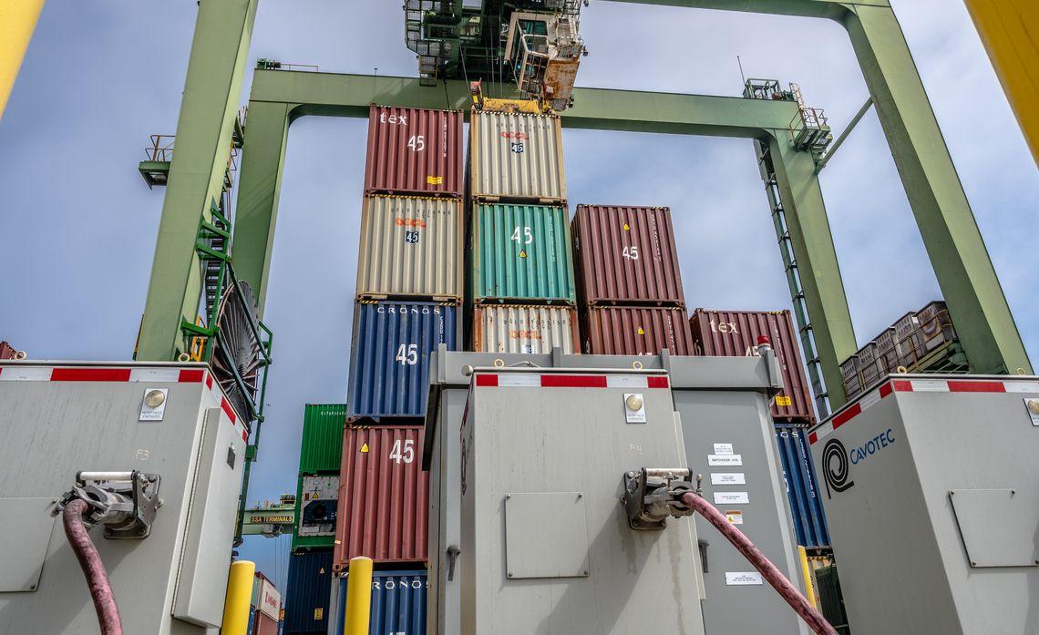 Stacked shipping containers and cranes, power boxes in front.