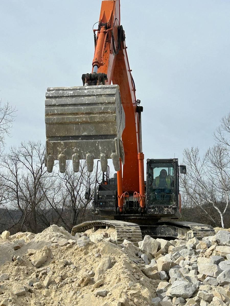 A large digging machine on top of a pile of rocks outside.