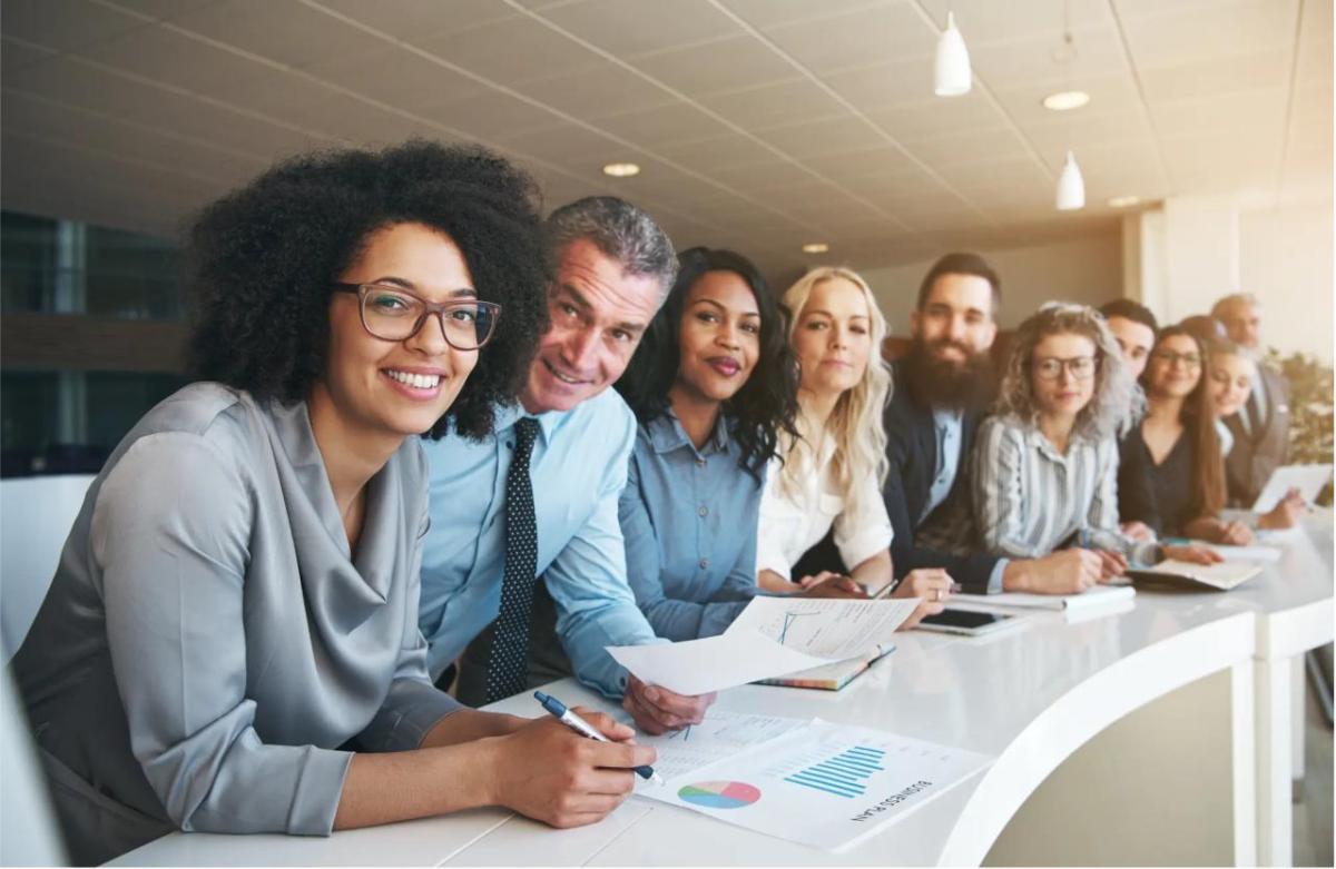 A row of diverse professionals at a long desk all looking at the camera.