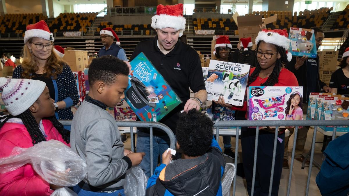 Volunteers in santa hats handing out toys to kids in a large auditorium.