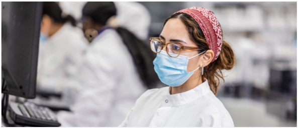 A person in ppe looking at a screen, others to their right doing the same