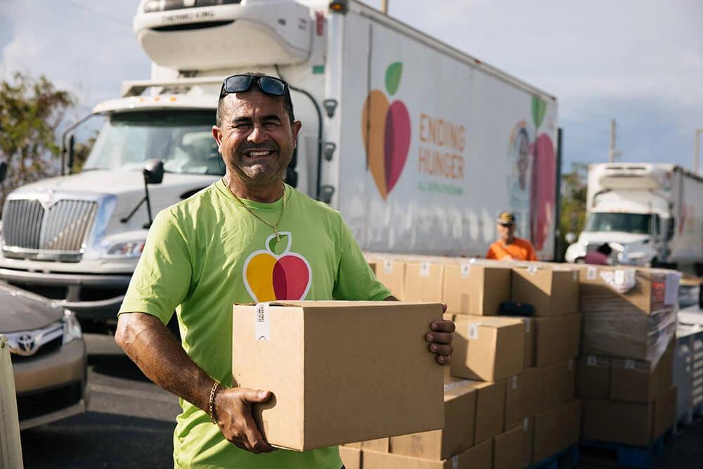 A person holding a box, a stack of boxes and truck behind them