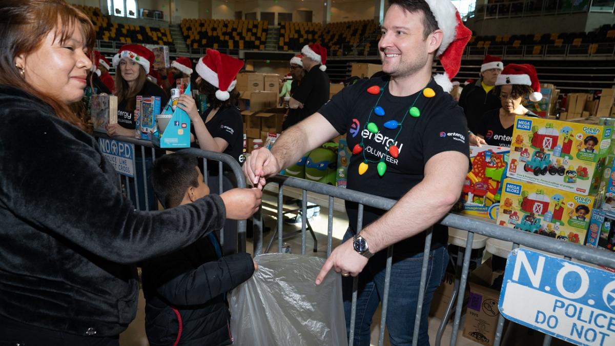 Volunteers in santa hats handing out toys to kids in a large auditorium.