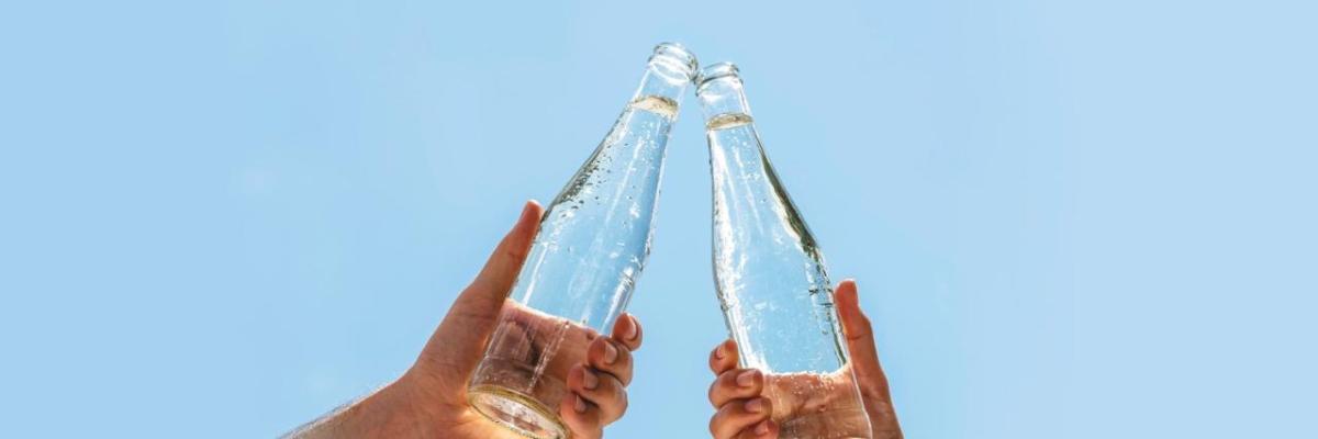 Two hands holding glass bottles, touching at the tops.