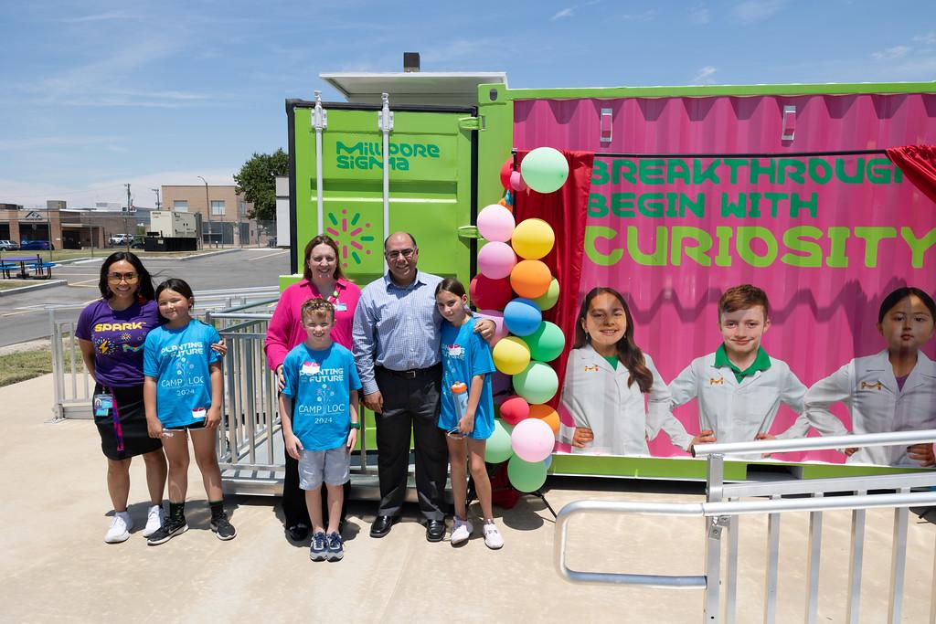 Three students and three adults stand next to their images featured on the Curiosity Cube.