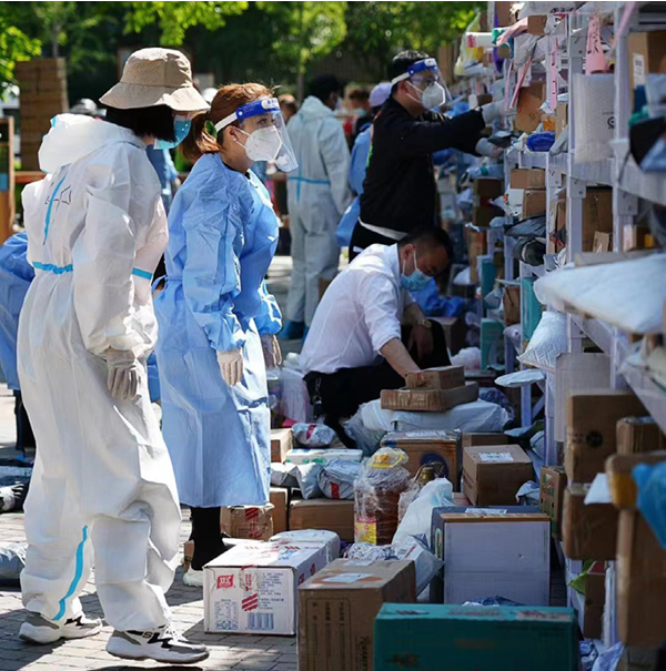 People in full ppe looking at shelves of boxes and other donations outside.