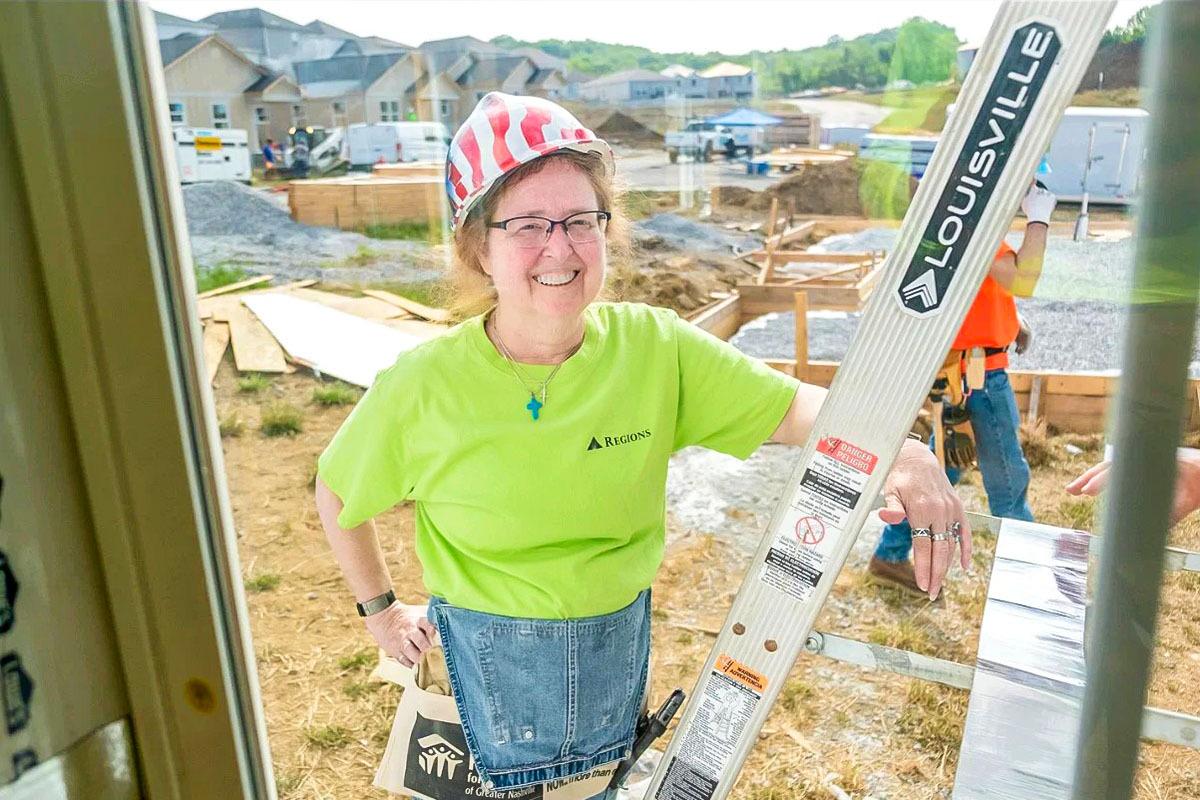 A smiling volunteer on a ladder.