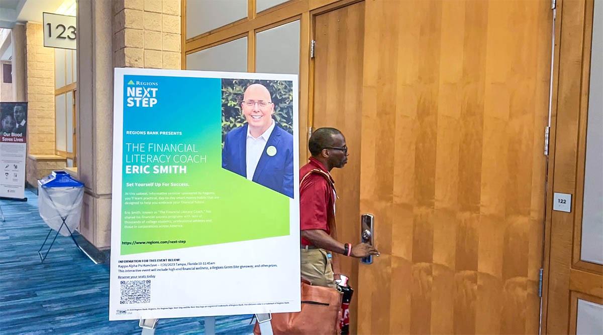 A person entering a meeting room. A sign for "The financial literacy coach" outside the door. 