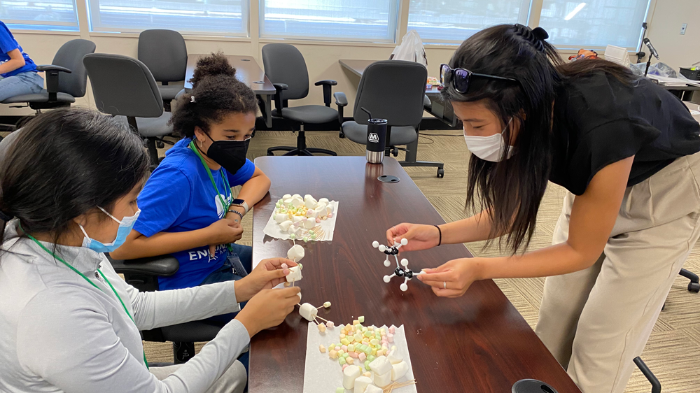 a staff member working with two children on a marshmallow molecule model