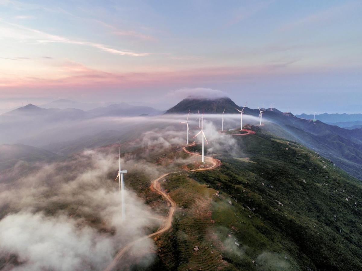 A winding path on a mountain ridge leading to multiple wind turbines.