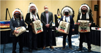 a group of five people, four wearing native american head coverings and carry woven blankets