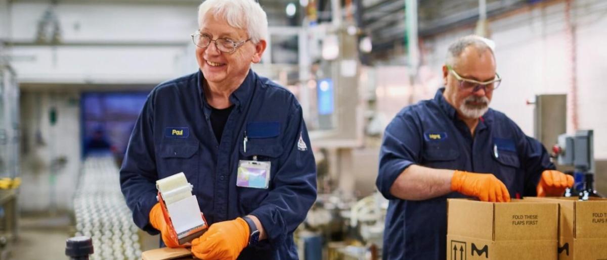 Two workers packaging products into boxes at a facility.