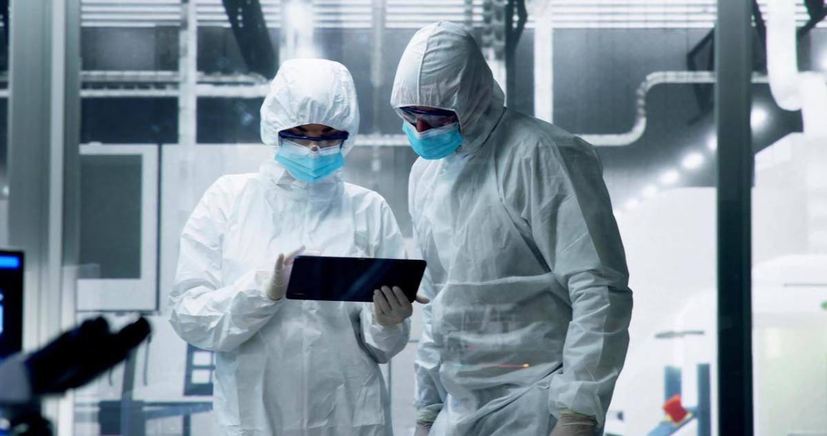 Two people in protective clothing looking at a tablet