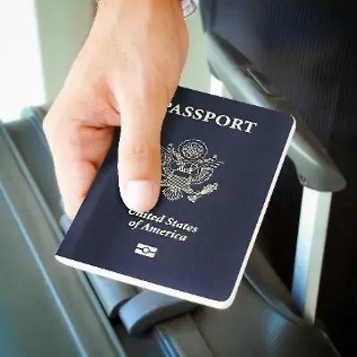 A hand holding out a US passport. Luggage leaning up against their leg.