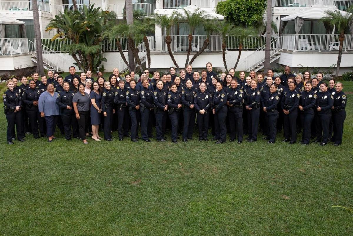 A large group of police officers in uniform and others posed in a grassy area.