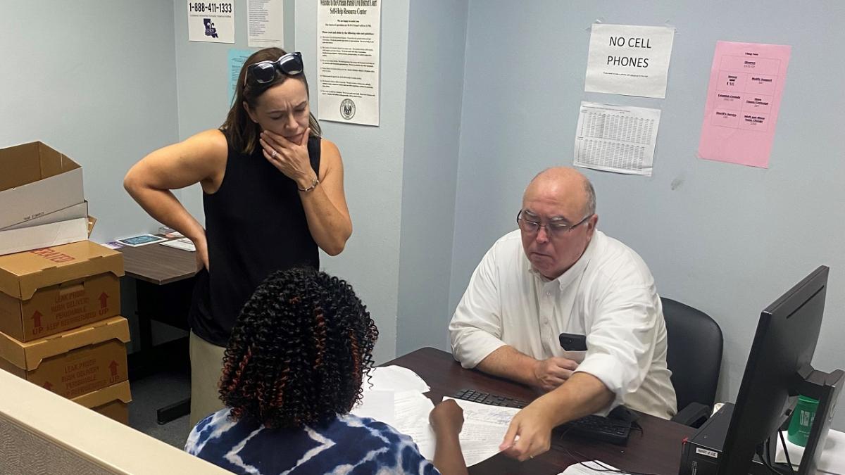 Two people sitting at a desk, a third looking on as they look at paperwork.