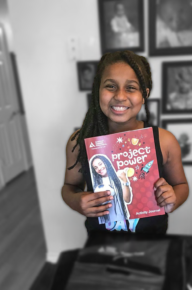 a child holds a book "project power" standing in front of a wall of family photos