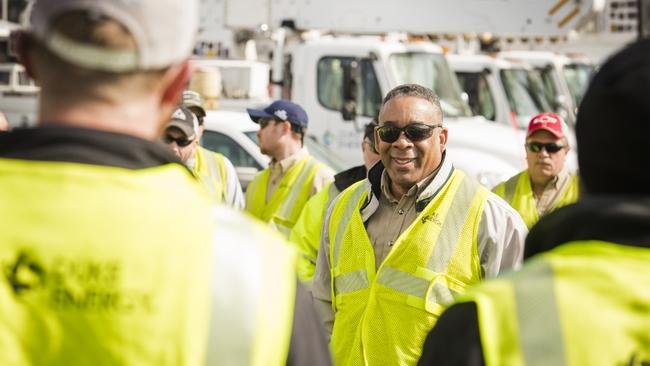 People gathered, all in high-vis vests. A row of utility trucks behind them.